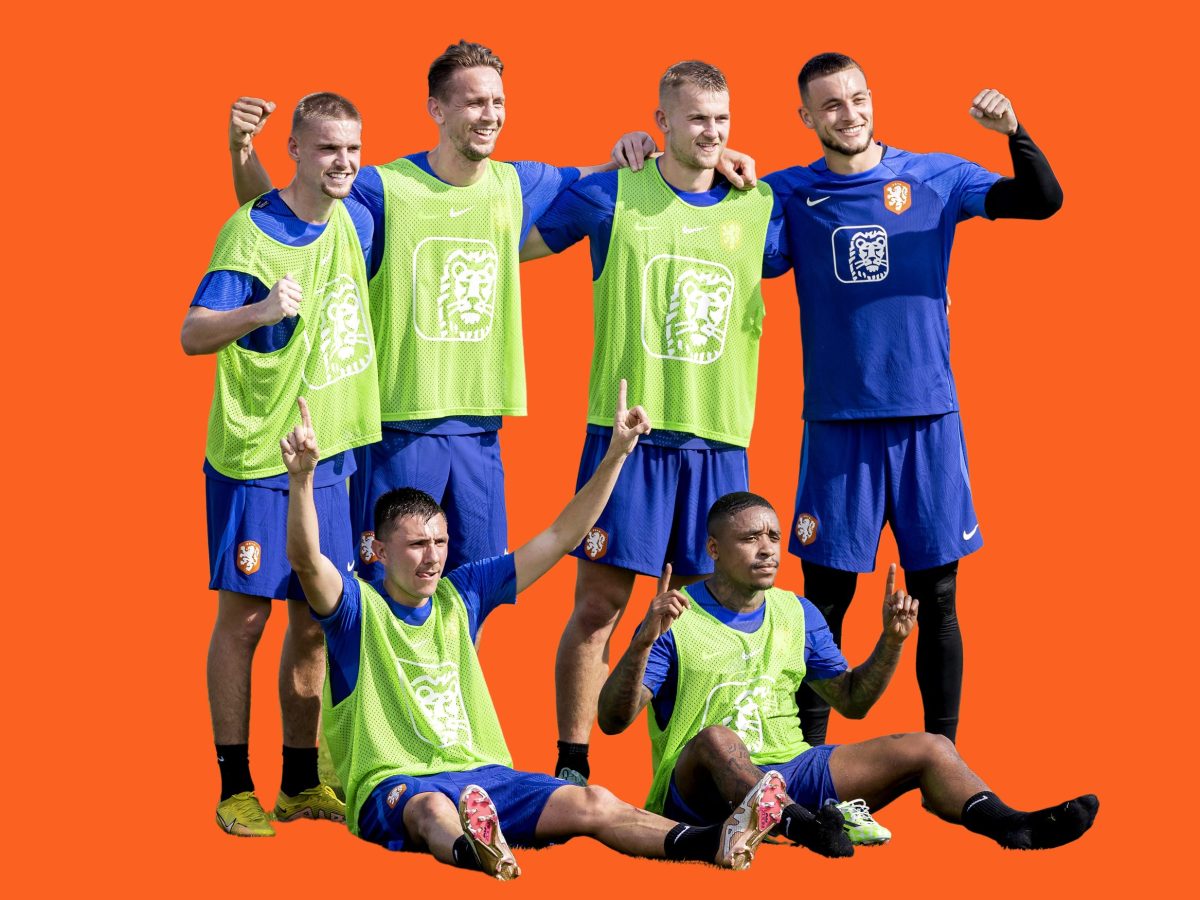 Six soccer players — four standing, two sitting — pose for a picture against a bright orange background.