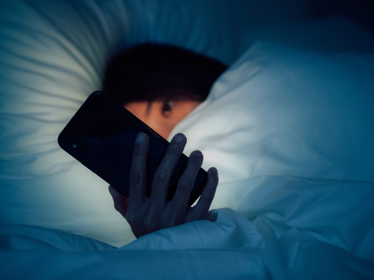 Woman hiding under the blanket, chatting and surfing the internet with smart phone at late night on bed.