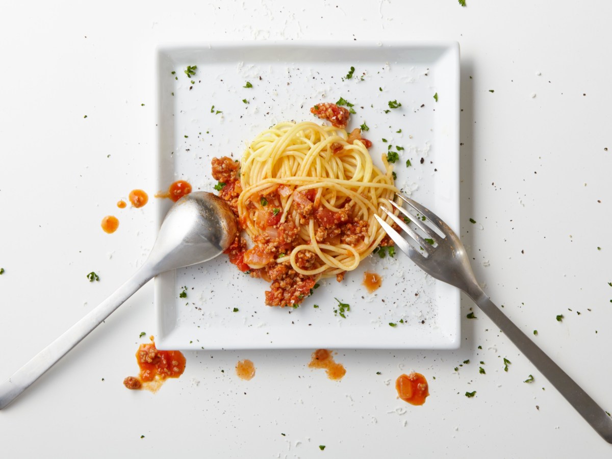 A messy dollop of pasta and sauce on a square white plate.